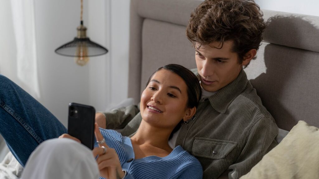 Par ser sammen på mobilen hjemme i sofaen