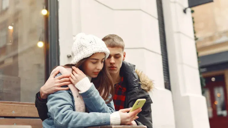 To ungdommer sitter tett sammen på en benk og ser på en mobiltelefon