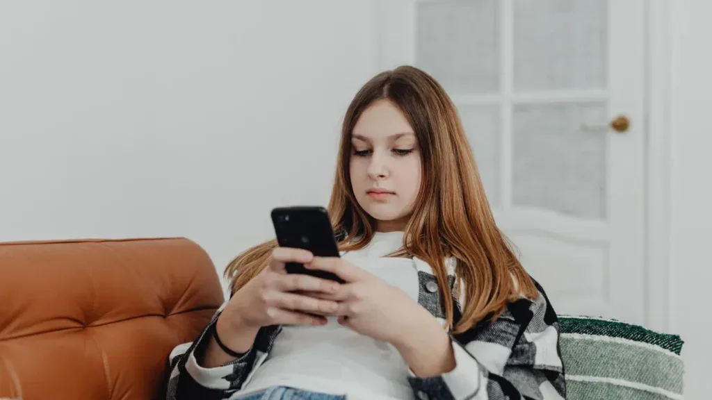 Ung jente sitter i en lenestol og ser på mobiltelefonen