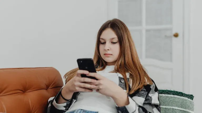 Ung jente sitter i en lenestol og ser på mobiltelefonen