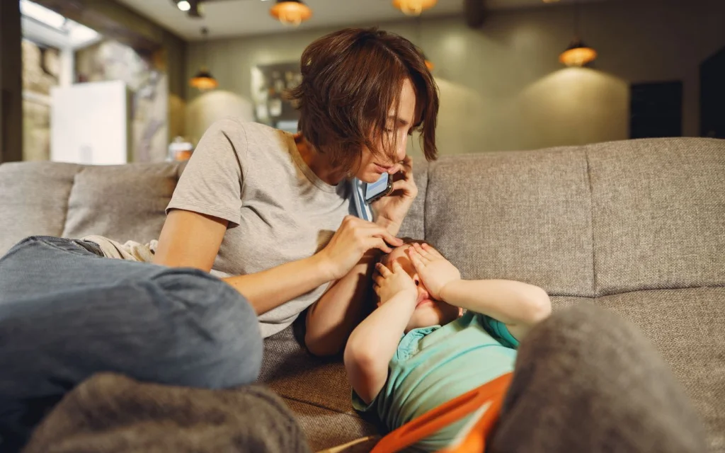 Mor med mobiltelefon sammen med barnet sitt i sofaen