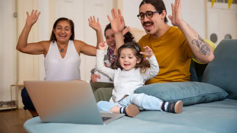 Familie på tre vinker til slektninger under en videosamtale hjemme i sofaen