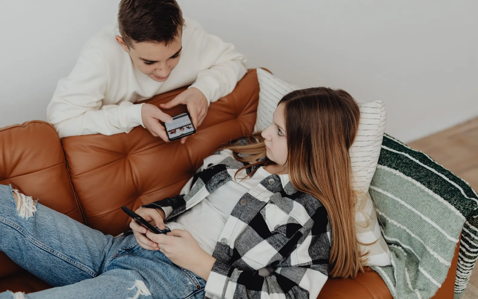 To ungdommer i sofaen med hver sin mobil